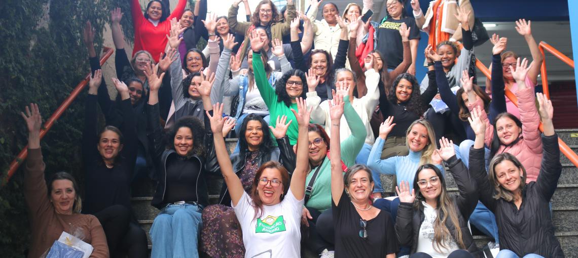Professoras sentadas levantando os braços