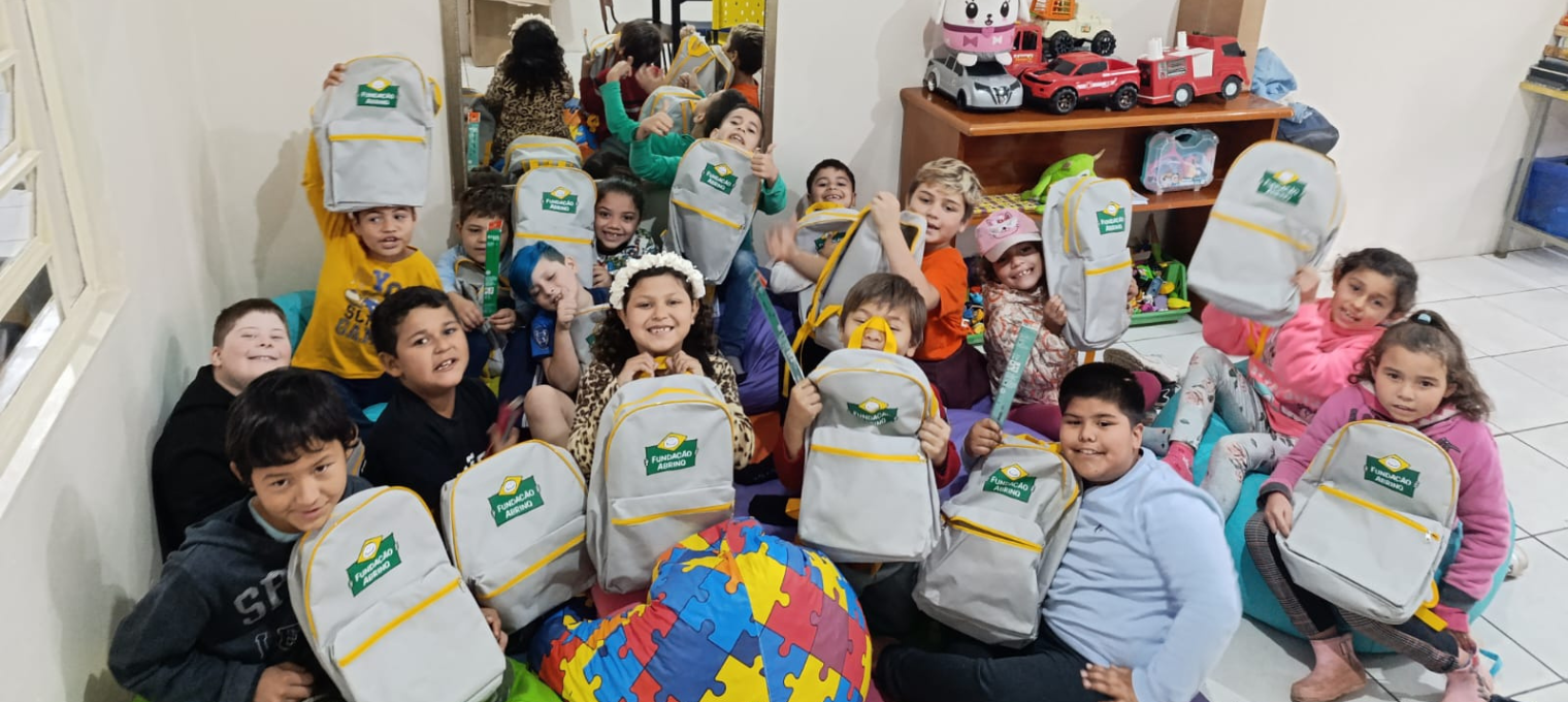 Crianças segurando mochila da Fundação Abrinq em um Espaço Seguro e Amigável