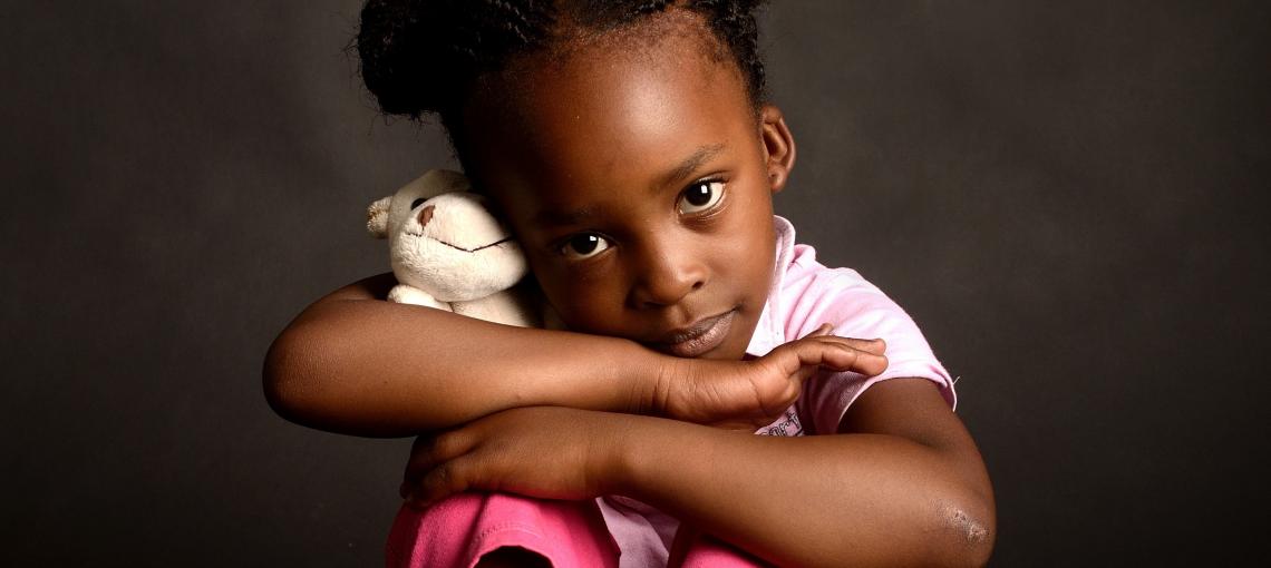 Criança sentada com pelúcia nos braços 